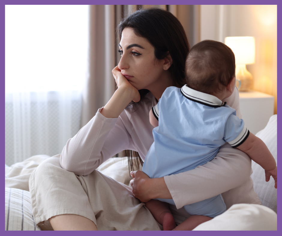 Persona adulta sentada en la cama, mirada pensativa, sosteniendo a un bebé de espaldas; lámpara encendida al fondo.