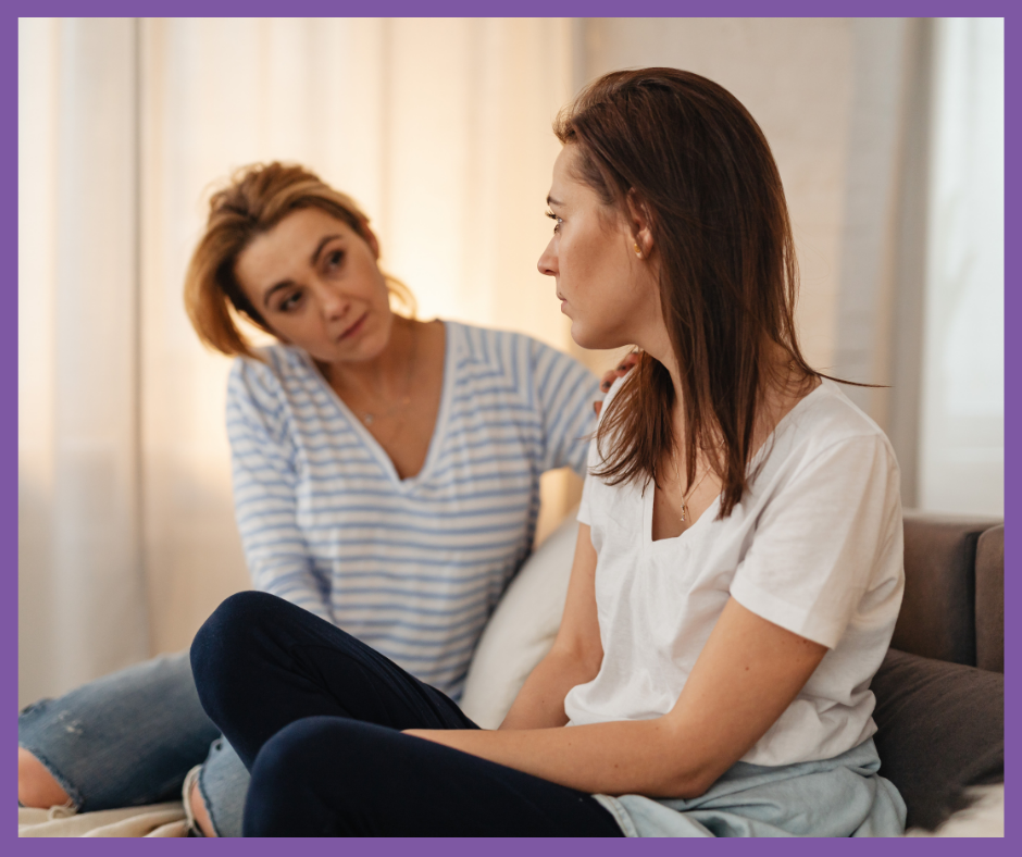 Dos personas adultas conversan en una sala; una escucha con atención y pone la mano en el hombro de la otra, que parece reflexiva o preocupada. Representa apoyo y empatía ante decisiones personales.